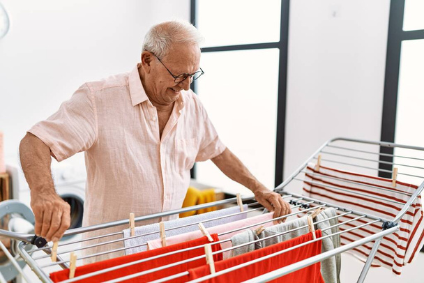 Uomo anziano sorridente fiducioso appeso vestiti su clothesline in lavanderia - Foto, immagini