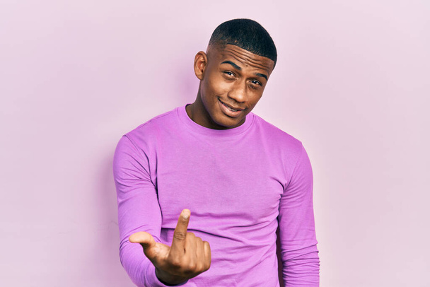 Молодий чорний чоловік в повсякденному рожевому светрі приходить сюди жест з рукою, запрошуючи привітний щасливий і усміхнений
  - Фото, зображення