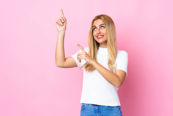 Молодая уругвайская блондинка на изолированном розовом фоне указывая указательным пальцем отличная идея - Фото, изображение