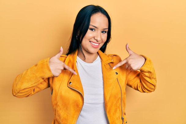 Mooie latino vrouw met neus piercing dragen geel lederen jas kijken zelfverzekerd met glimlach op het gezicht, wijzend zichzelf met vingers trots en gelukkig.  - Foto, afbeelding