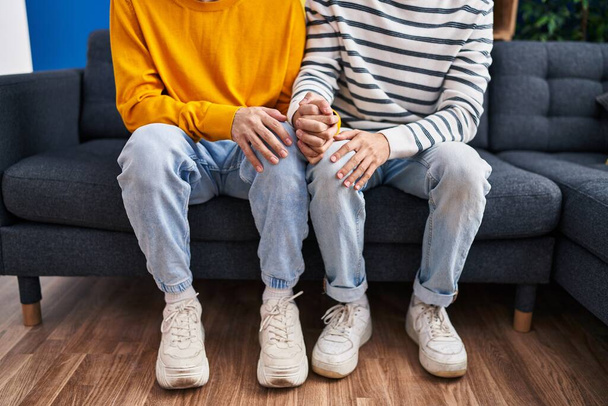 Two man couple sitting on sofa with hands together at home - Фото, изображение