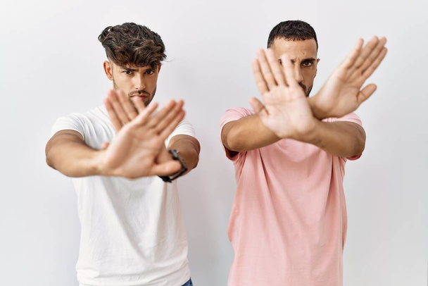 Young gay couple standing over isolated background rejection expression crossing arms and palms doing negative sign, angry face  - Photo, Image