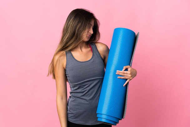 Young sport woman going to yoga classes while holding a mat isolated on pink background with sad expression - Fotoğraf, Görsel
