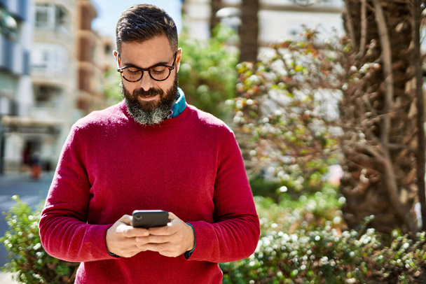 Junger hispanischer Geschäftsmann lächelt glücklich mit Smartphone in die Stadt. - Foto, Bild