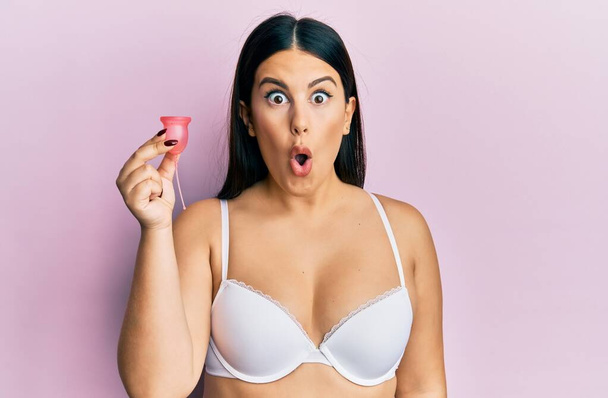 Krásná brunetka žena drží menstruační pohár na sobě spodní prádlo mrkání do kamery se sexy výraz, veselý a šťastný obličej.  - Fotografie, Obrázek