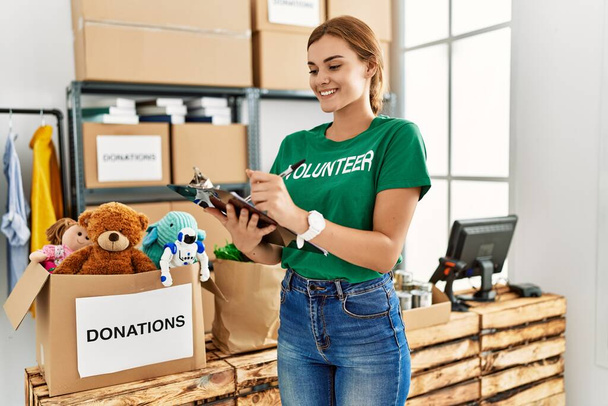 Junge Frau trägt freiwillige Uniform mit Schriftzug auf Klemmbrett im Charity Center - Foto, Bild