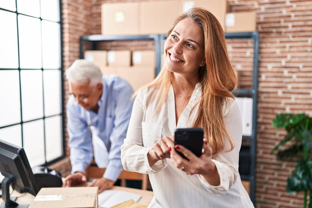 Hombre y mujer de mediana edad comercio electrónico de los trabajadores de negocios utilizando el teléfono inteligente en la oficina - Foto, imagen