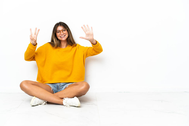 Mladá žena sedí na podlaze izolované na bílém pozadí počítání osm s prsty - Fotografie, Obrázek