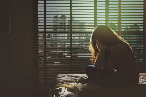 depresivní žena sedí hlavu v rukou na posteli v temné ložnici s nízké hladiny osvětlení prostředí, dramatický koncept - Fotografie, Obrázek