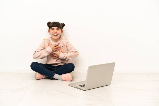 Little girl with a laptop sitting on the floor smiling a lot - Photo, Image