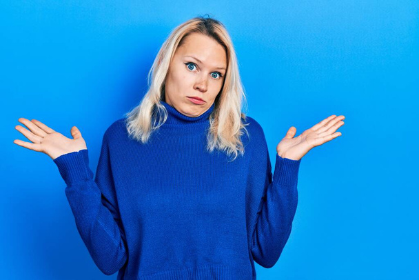 Beautiful caucasian blonde woman wearing turtleneck sweater clueless and confused with open arms, no idea and doubtful face.  - Foto, imagen