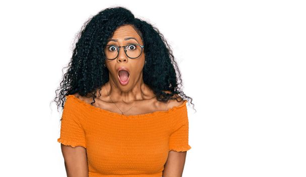 Mujer afroamericana de mediana edad vistiendo ropa casual y gafas asustada y sorprendida con expresión sorpresa, miedo y cara excitada.  - Foto, Imagen
