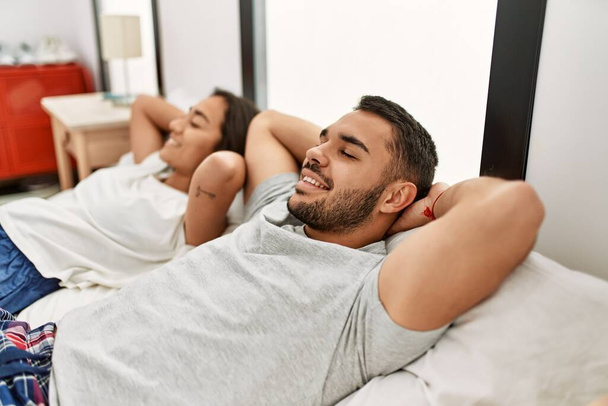 Nuori latino pari rentouttava kädet päällä makaa sängyssä kotona. - Valokuva, kuva