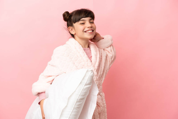 Little caucasian girl isolated on pink background in pajamas and holding a pillow and yawning - 写真・画像