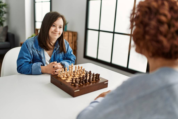 Mature mother and down syndrome daughter playing chess boardgame at home - Photo, Image