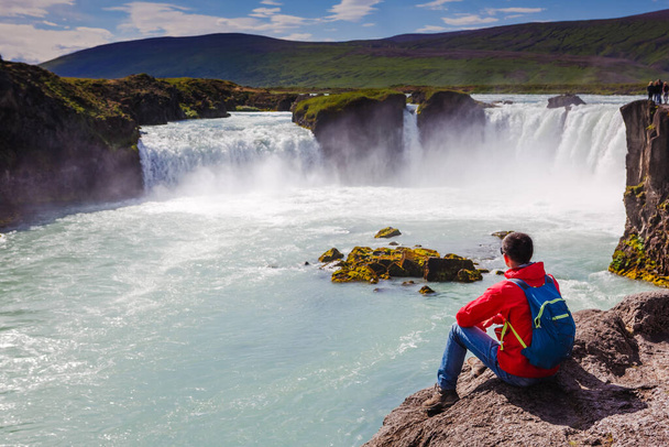Man in red jacket looking at Godafoss waterfall. Beautiful landscape in Iceland - Fotoğraf, Görsel