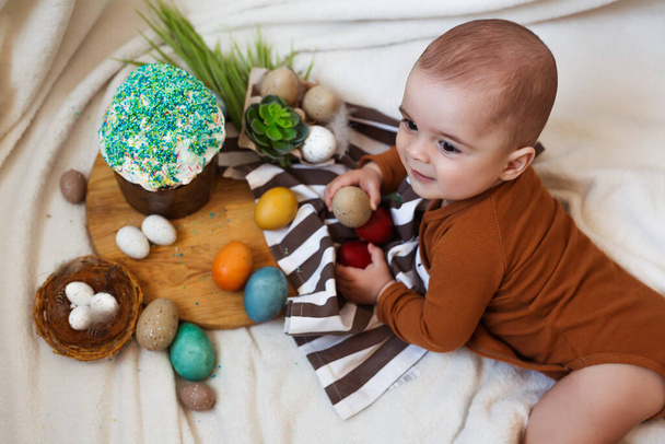 Happy Easter. Cute and happy little baby playing with Easter eggs and cake at home. - Photo, Image