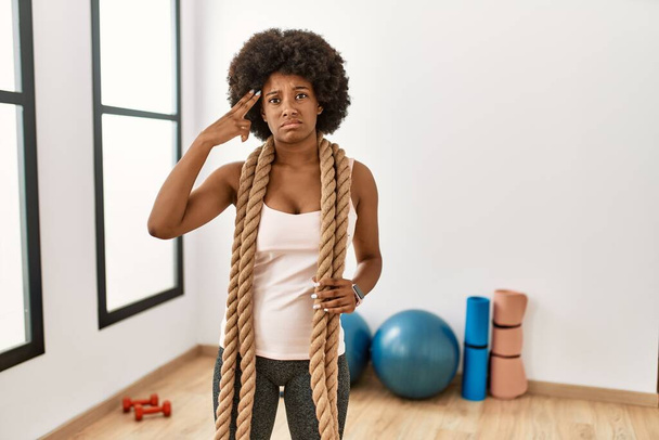 Young african american woman with afro hair at the gym training with battle ropes shooting and killing oneself pointing hand and fingers to head like gun, suicide gesture.  - Photo, Image