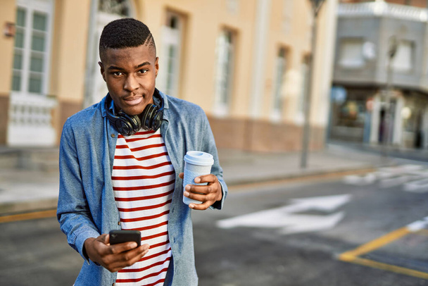 Молодий афроамериканець, користуючись смартфоном, п "є каву в місті.. - Фото, зображення