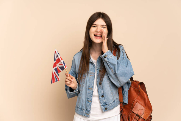 Junge Ukrainerin mit einer britischen Flagge auf beigem Hintergrund, die mit weit geöffnetem Mund schreit - Foto, Bild