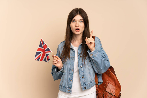 Junge Ukrainerin mit einer britischen Flagge auf beigem Hintergrund, die die Lösung erkennen will, während sie den Finger hebt - Foto, Bild