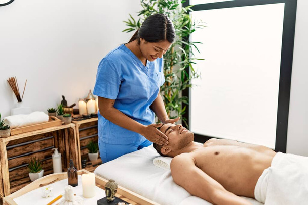 Joven masaje latino terapeuta mujer dando un tratamiento relajante en la cabeza del hombre en el centro de belleza. - Foto, imagen