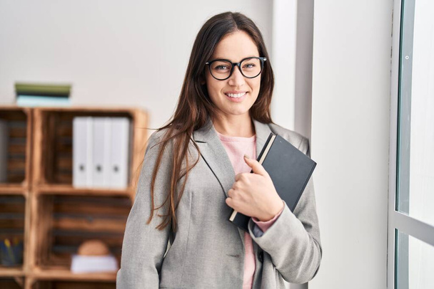 Young woman psychologist smiling confident holding book at psychology center - Φωτογραφία, εικόνα