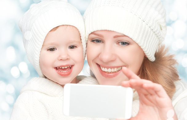 selfie en invierno. feliz familia madre con hija y fotografiado uno mismo en el teléfono móvil
 - Foto, Imagen