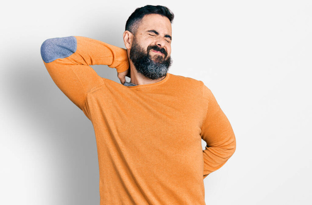 Hombre hispano con barba vistiendo suéter casual de invierno sufriendo de lesión en el cuello, tocando el cuello con la mano, dolor muscular  - Foto, imagen