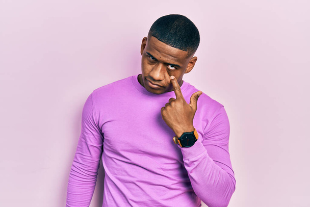 Молодий чорний чоловік в повсякденному рожевому светрі вказує на око, спостерігаючи за вашим жестом, підозрілий вираз
  - Фото, зображення