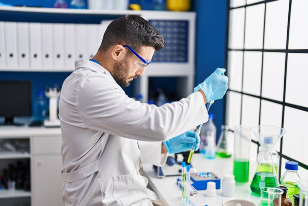 Junger hispanischer Mann in Wissenschaftleruniform misst Flüssigkeit im Labor - Foto, Bild