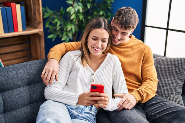 Young man and woman couple using smartphone sitting on sofa at home - Photo, image