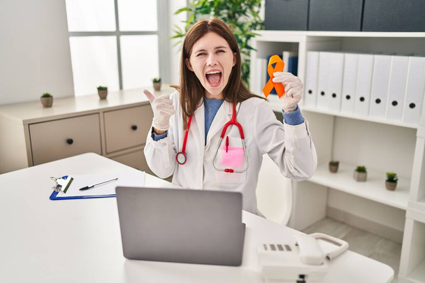 Elinde turuncu kurdele tutan genç bir doktor kadın başparmağıyla ağzını açıp gülümsüyor.  - Fotoğraf, Görsel