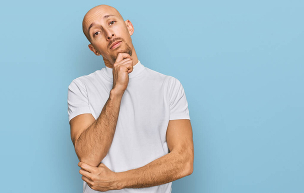 Bald man with beard wearing casual white t shirt looking confident at the camera with smile with crossed arms and hand raised on chin. thinking positive.  - 写真・画像