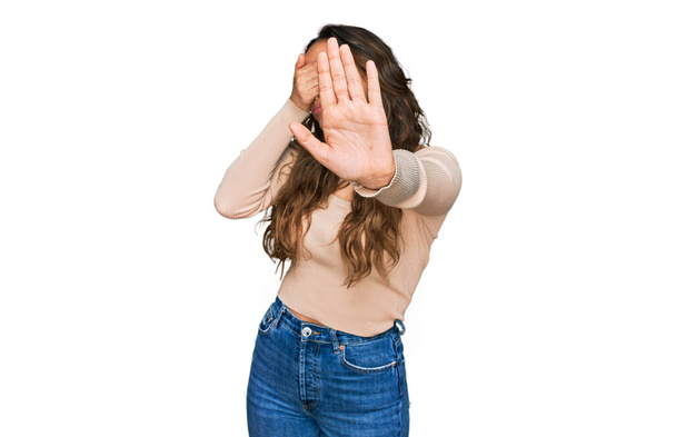 Молода іспаномовна дівчина носить повсякденний одяг, прикриваючи очі руками і роблячи стоп жест з сумним і страшним виразом. збентежена і негативна концепція
.  - Фото, зображення