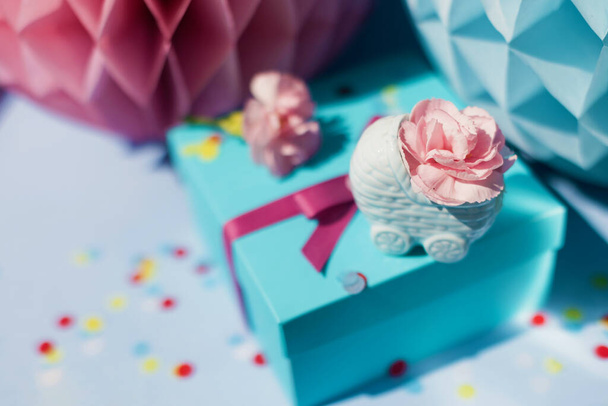 Гендер розкриває вечірку з рожевими і синіми прикрасами на синьому фоні. Хлопчик або дівчинка вечірка. Синя коляска з рожевими квітами, подарункова коробка зі стрічкою та великими паперовими кульками
 - Фото, зображення