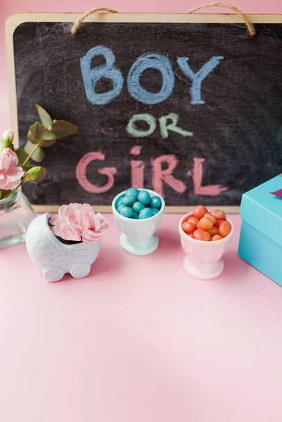 Kreidetafel mit Schild BOY OR GIRL, blaue Kinderwagen-Vase mit rosa Blüten, blauen und rosa Bonbons und anderen Dekorationen. Gender-Party mit rosa und blauen Dekorationen auf rosa Hintergrund. Jungen- oder Mädchenparty - Foto, Bild