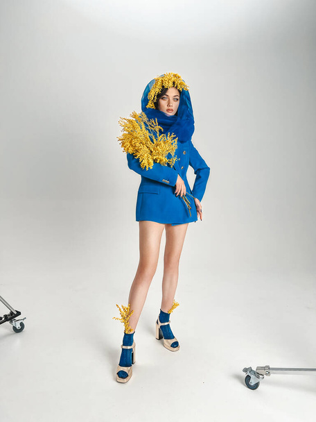 Chica joven en una chaqueta azul y chales con un ramo de mimosa en el estudio  - Foto, Imagen