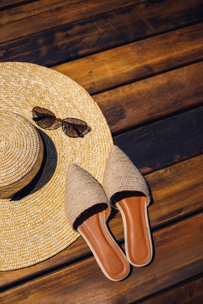 Sommermütze, Sonnenbrille und Pantoletten liegen auf einem hölzernen Hintergrund. Platz für eine Inschrift oder Werbung - Foto, Bild