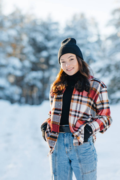 Onnellinen nuori hymyilevä nainen kävelee metsässä lumen peitossa mäntyjä aurinkoisena talvipäivänä. - Valokuva, kuva