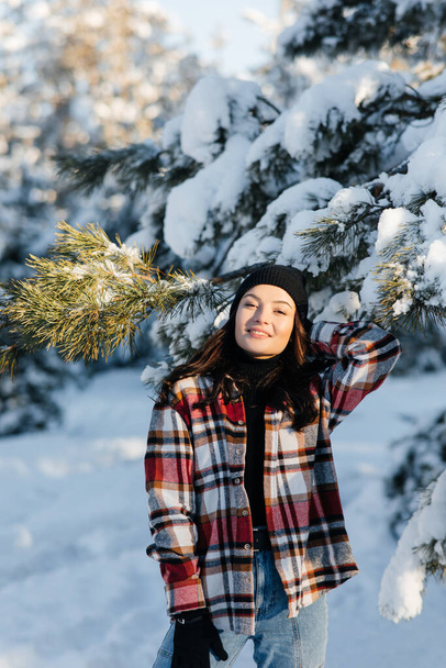 Happy young smiling woman walks in forest among snow covered pine trees in sunny winter day. - Φωτογραφία, εικόνα