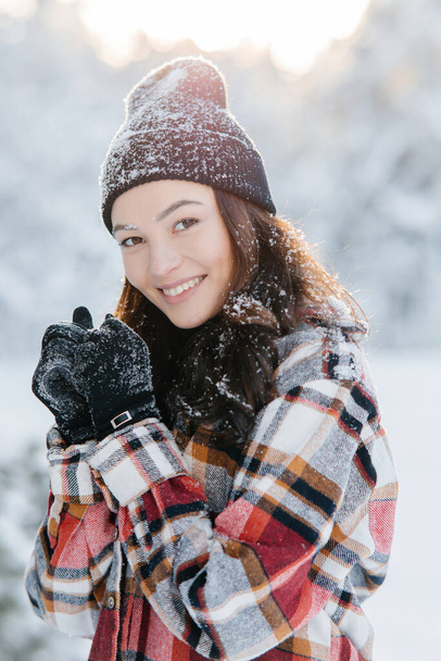 Porträt einer jungen glücklich lächelnden Frau mit schneebedeckter Kleidung bei einem Waldspaziergang an einem sonnigen Wintertag. - Foto, Bild