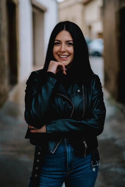 portrait of a beautiful young woman in a black leather jacket and jeans posing on the street - Fotografie, Obrázek