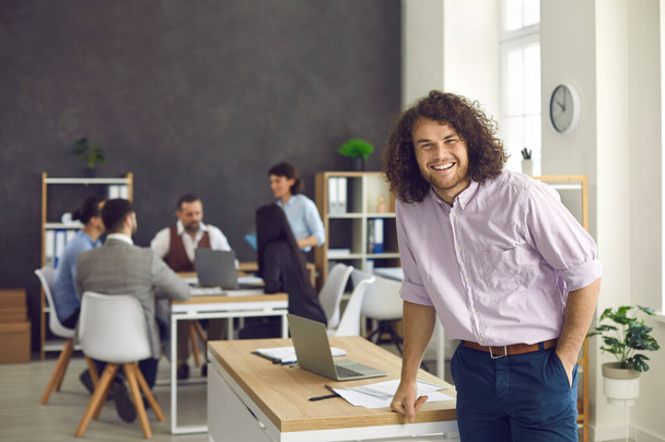 Cheerful young businessman looking at camera with smile standing in office - Foto, Bild