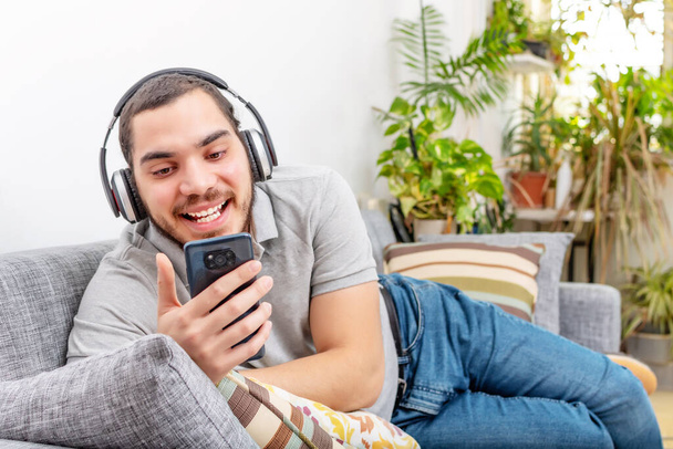 young man listening to music on sofa at home - Foto, imagen