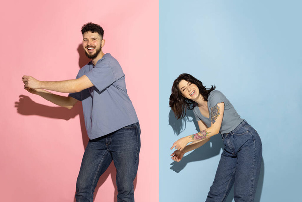 Young excited couple of funny and happy man and girl dancing hip-hop, having fun isolated on blue and pink trendy color background. Emotions concept - Foto, Bild
