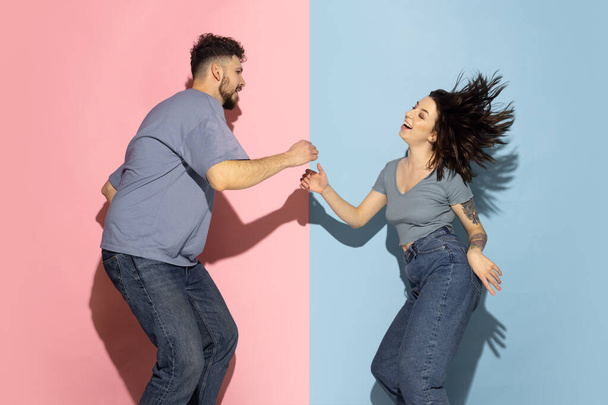 Young excited couple of funny and happy man and girl dancing hip-hop, having fun isolated on blue and pink trendy color background. Emotions concept - Valokuva, kuva