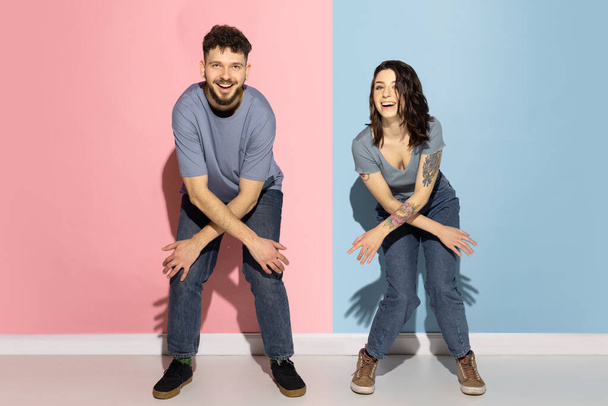 Young excited couple of funny and happy man and girl dancing hip-hop, having fun isolated on blue and pink trendy color background. Emotions concept - Foto, afbeelding