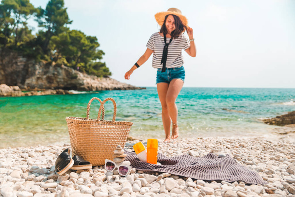 Strandsachen Strohhut und Tasche mit Flossen und Sonnenschutzcreme an der Küste Frau im Hintergrund - Foto, Bild