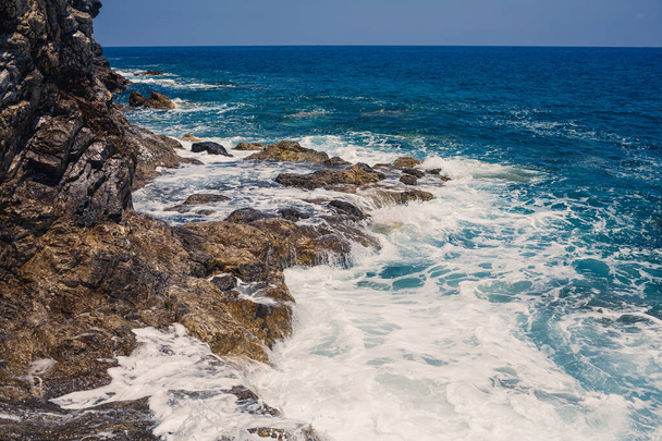 Mavi Akdeniz 'in harika manzarası. Güneşli kayalar, köpüklü dalgalar ve su sıçraması. Dalga kıyıdaki kayalara çarpar. - Fotoğraf, Görsel